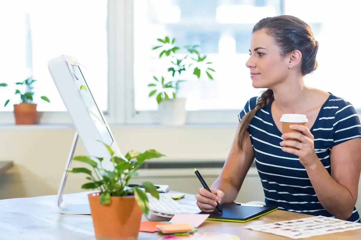 Smiling casual businesswoman working on digitizer and holding coffee