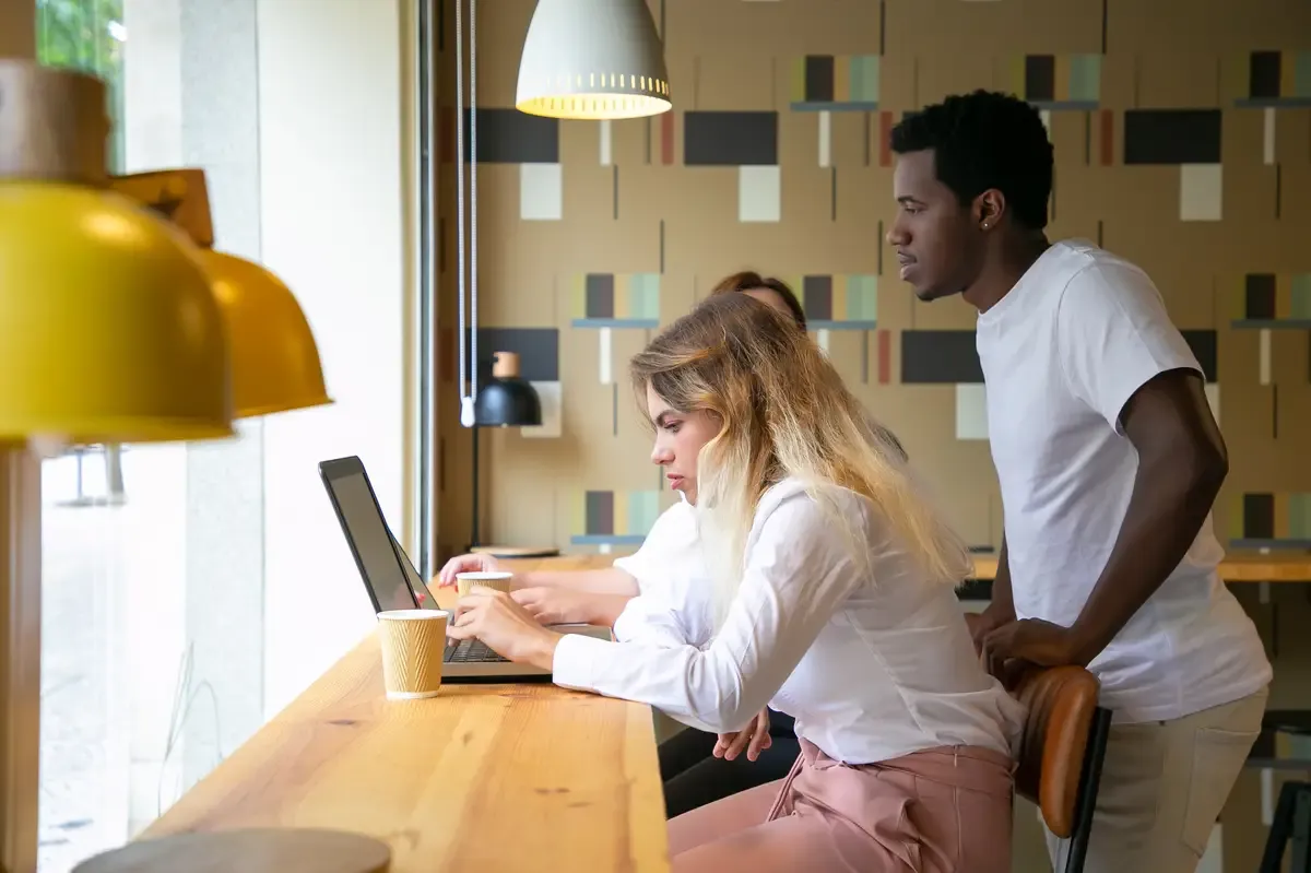 African American guy standing behind blonde woman and looking at screen